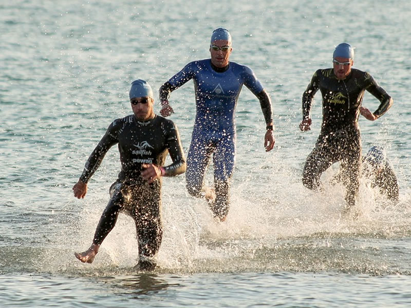 L'immagine mostra tre nuotatori che intenti ad uscire dall'acqua e guadagnare la riva in corsa